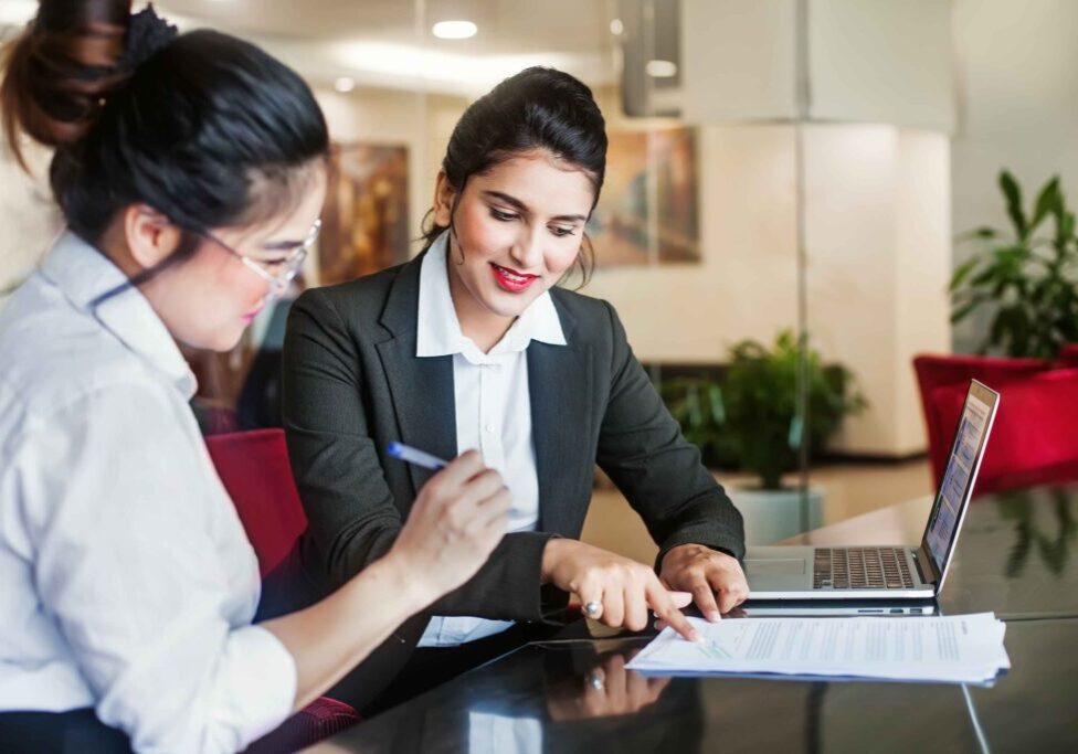 Two women discussing documents at desk.
